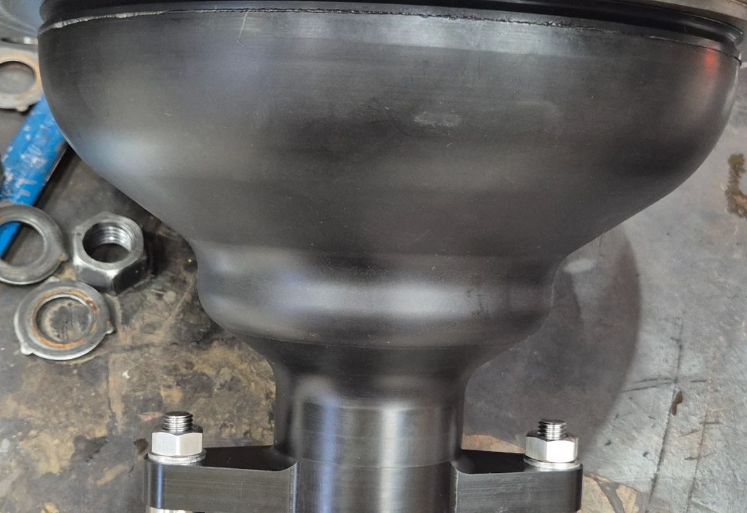 Black bell-shaped seal body pressed against the underside of a steel flange, held by a clamp yoke on stainless studs