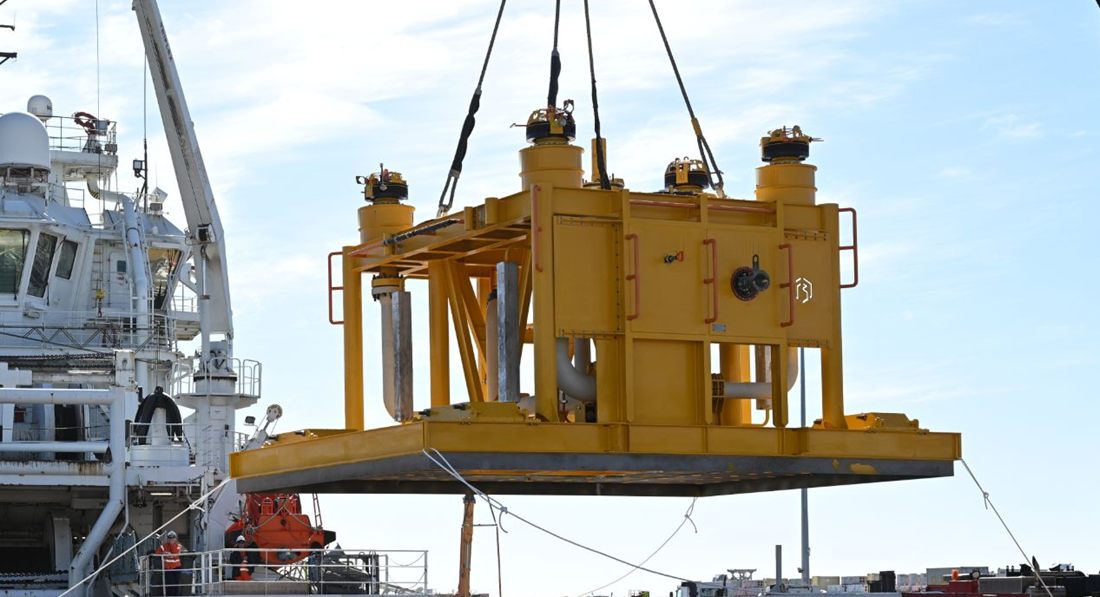 Yellow Blakemere subsea manifold on its mudmat base, lifted by crane over the deck of an offshore vessel while crew steady it with tag lines