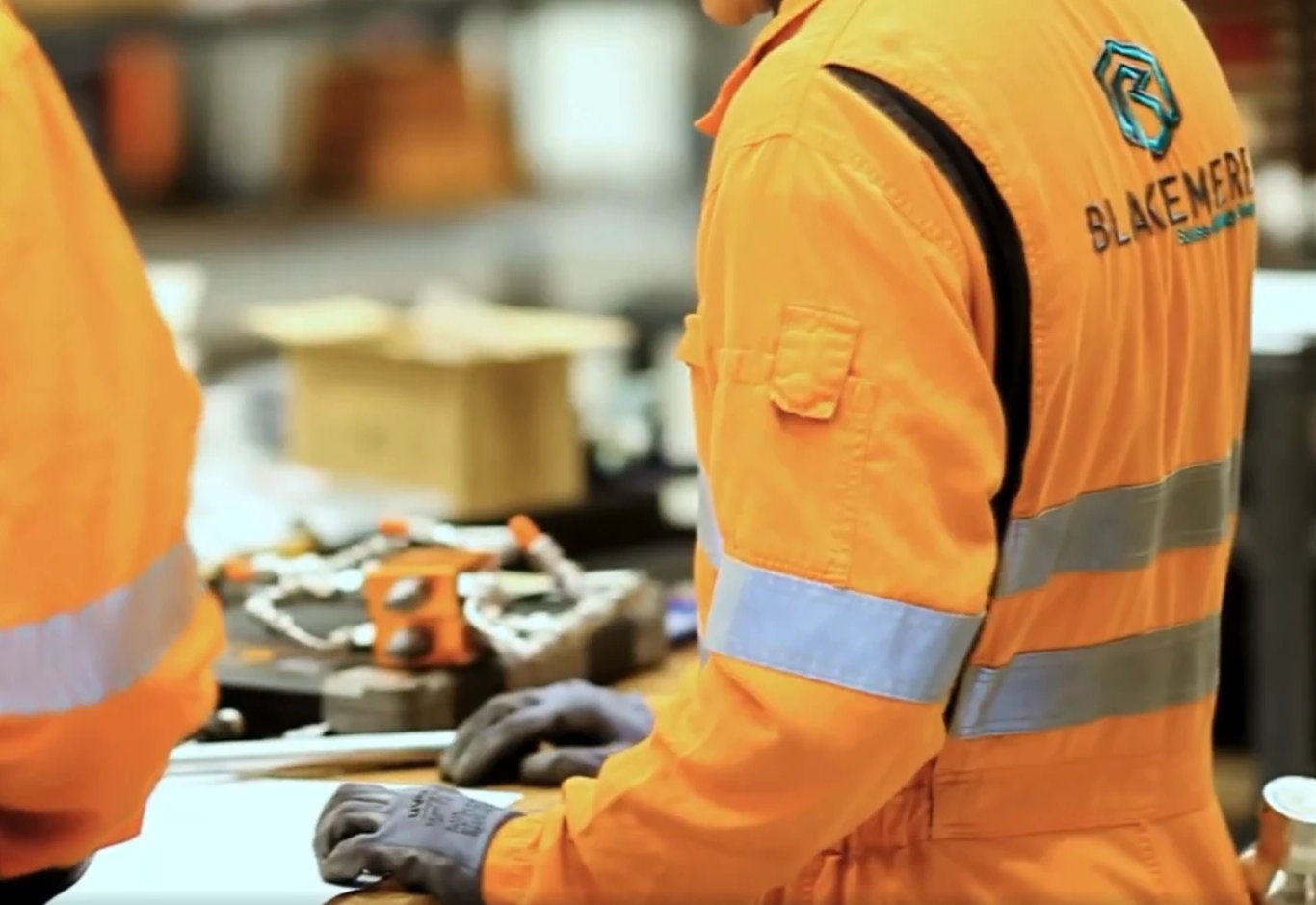 Two Blakemere technicians in branded coveralls working at a workshop bench, tooling laid out in front of them