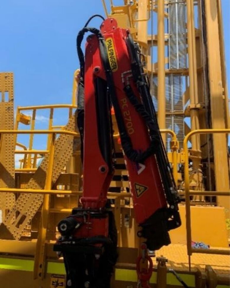A Palfinger PC 2700 knuckle boom crane stowed upright beside the rig mast.