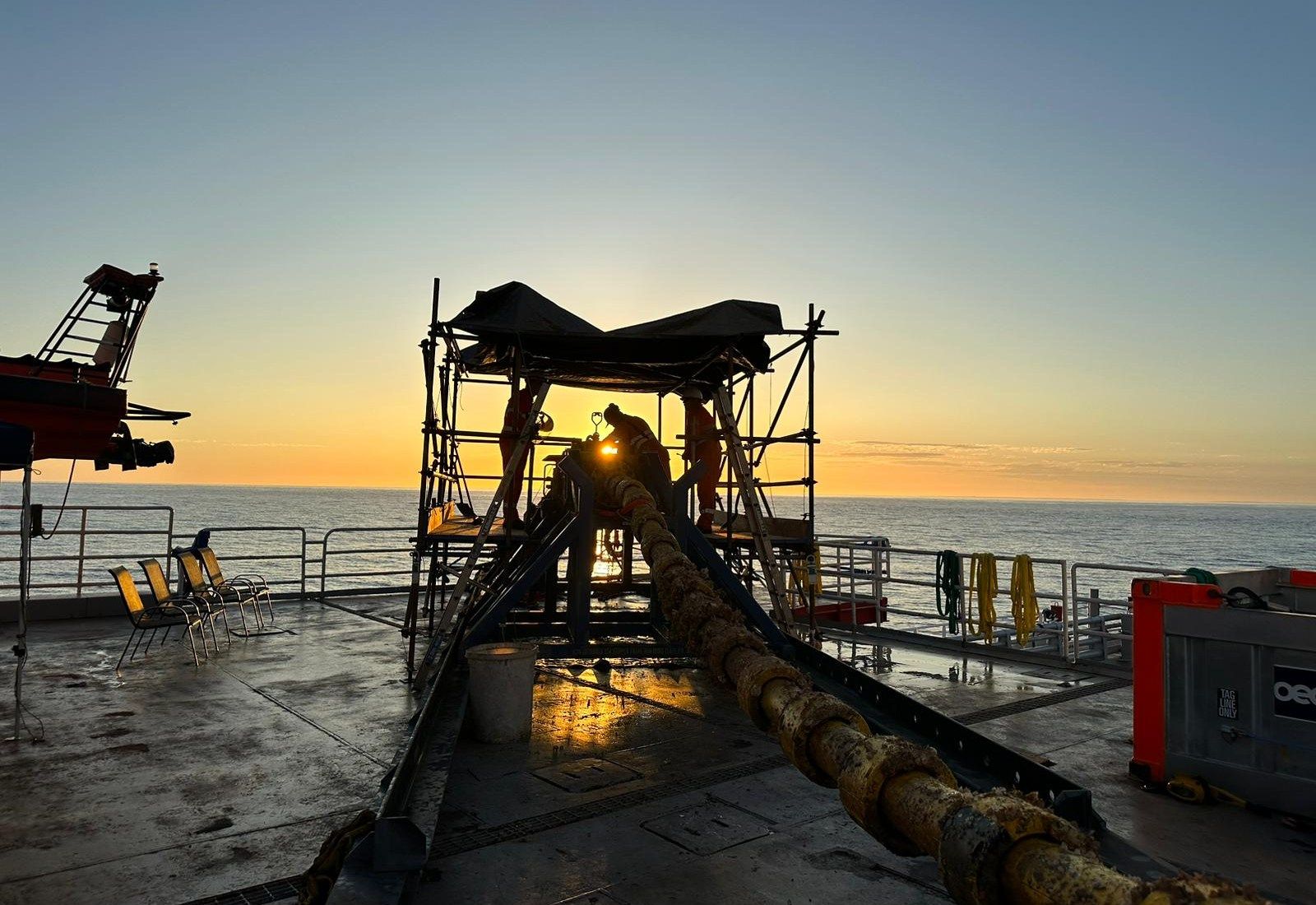 A marine-growth-covered line running up a deck chute into a scaffolded work habitat at first light