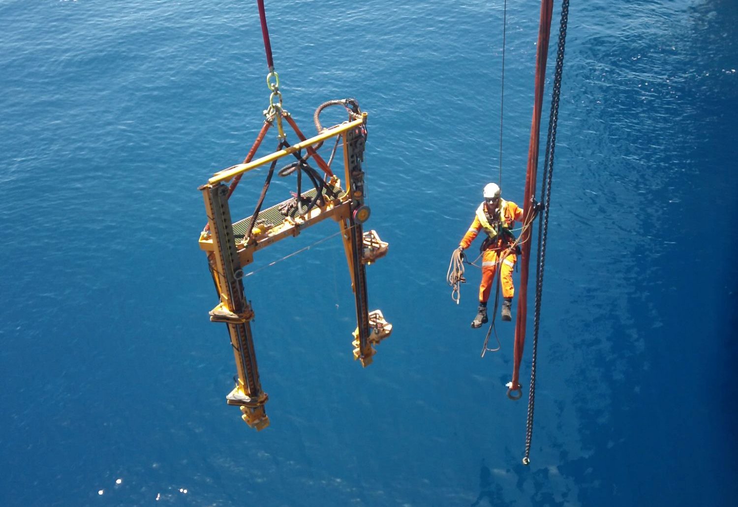 A Blakemere subsea deployment frame on the crane wire above open water, a rope access technician alongside on the lift lines