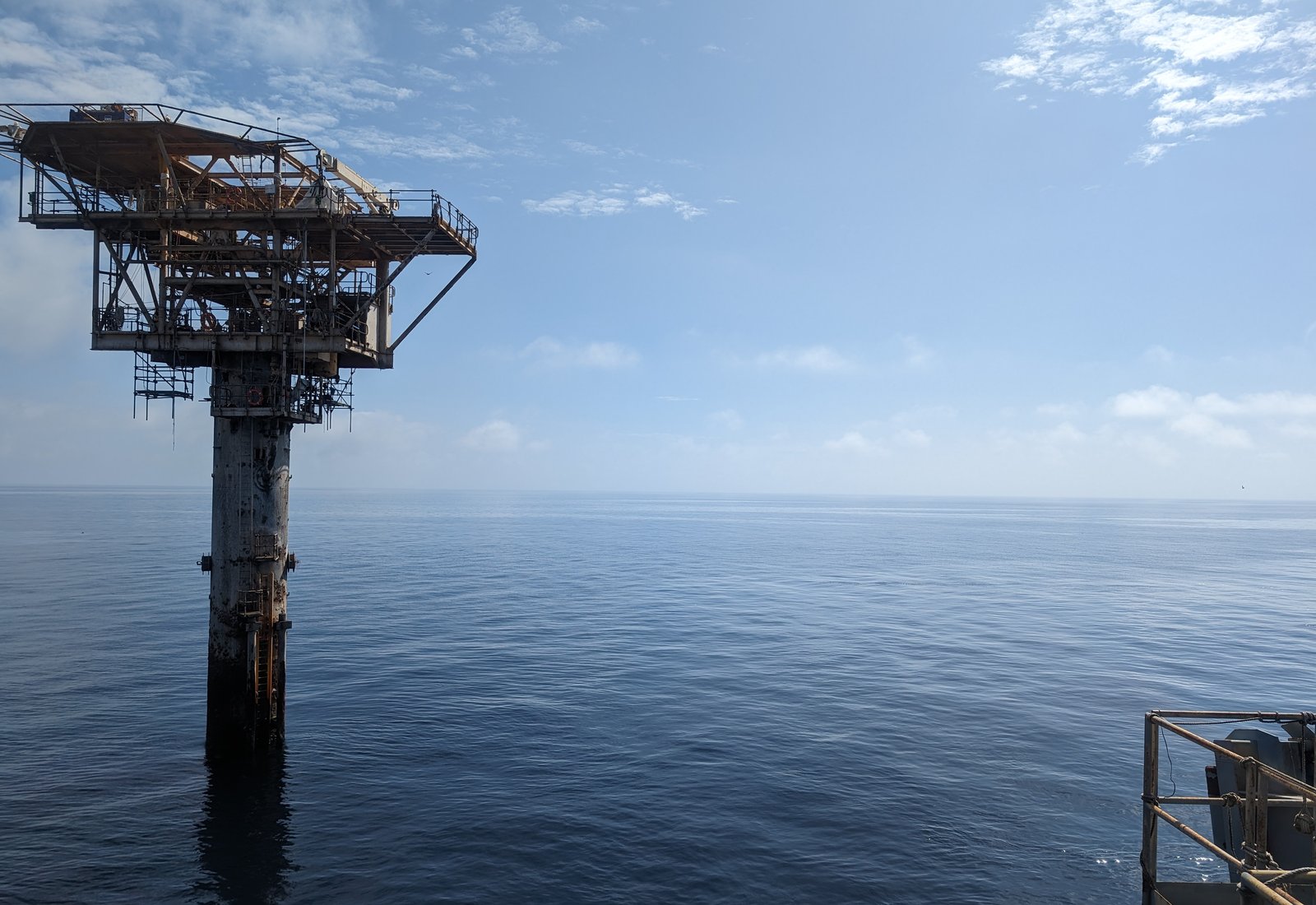An unmanned monopod platform standing in calm water, seen from the deck of a work vessel